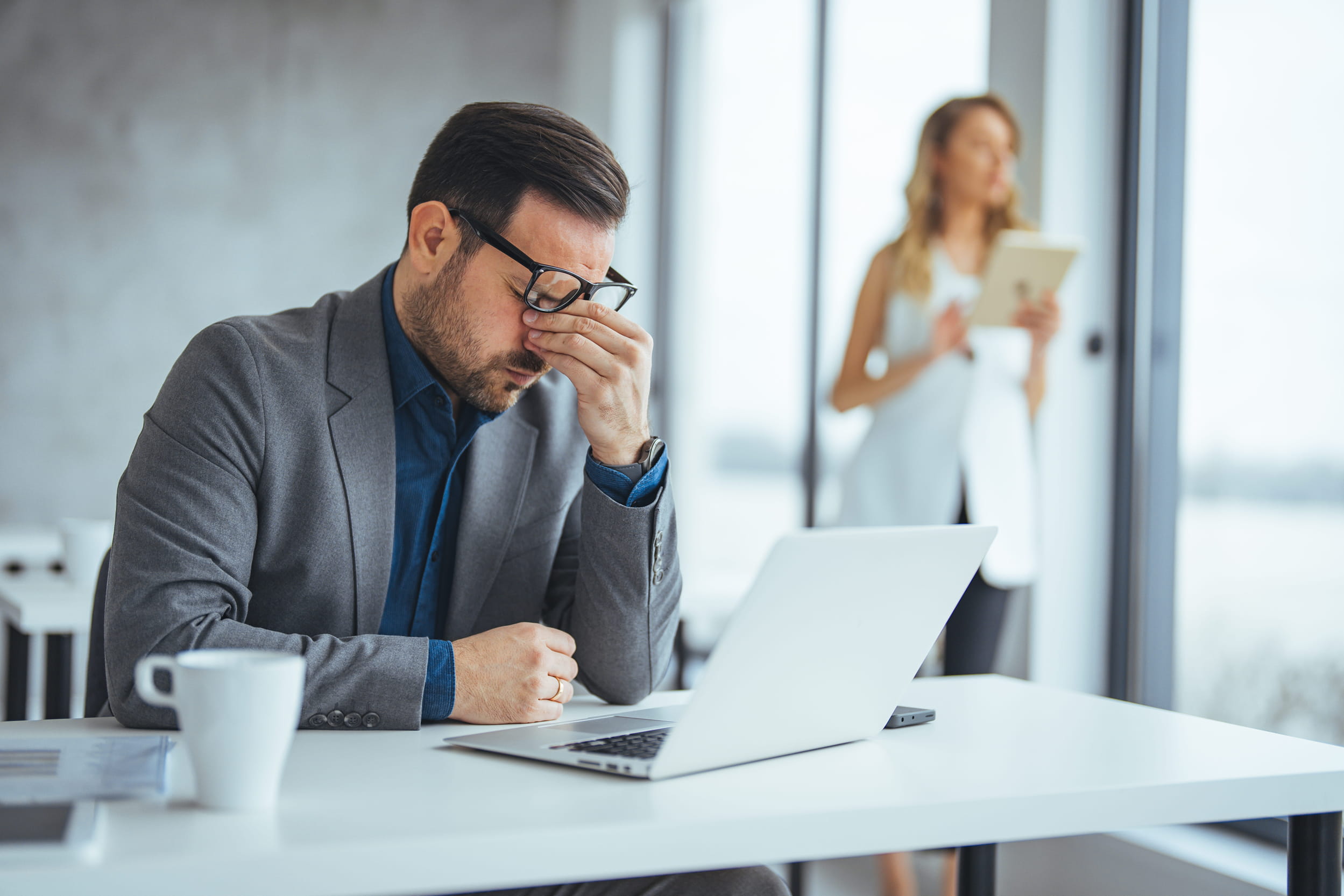 Stressed businessman rubbing his eyes at a laptop in an office, illustrating the impact of chronic stress on wellbeing and the need for holistic stress management